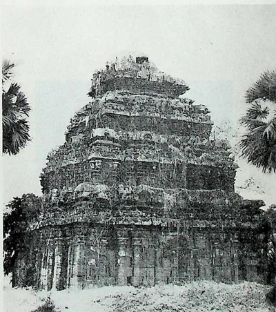 A small stone temple with a heavy, weathered pyramidal tower of several tiers, standing in scrub with palms behind.