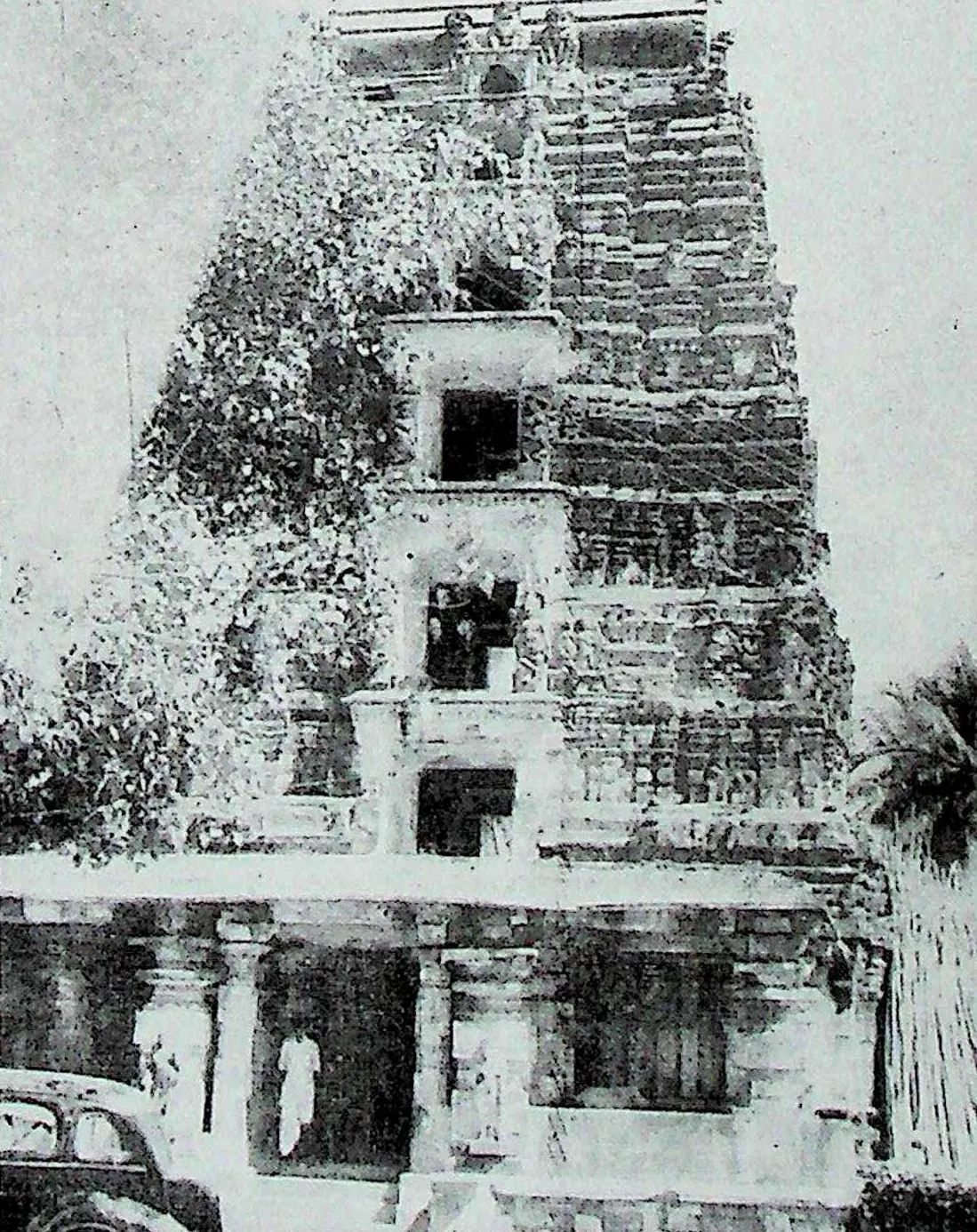 A tall gateway tower of several storeys with openings in the centre of each, rising above a pillared entrance; a car and a few people at its foot.