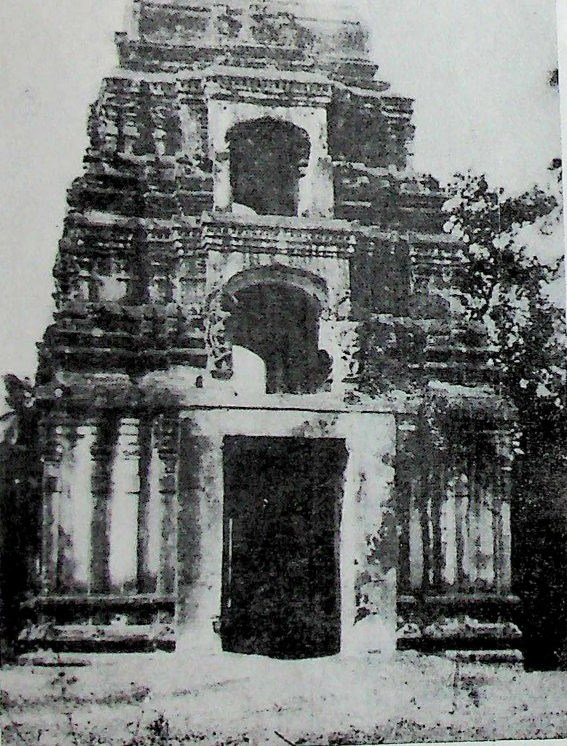 A massive weathered gateway tower with a large doorway at the base and arched openings above, with trees on both sides.