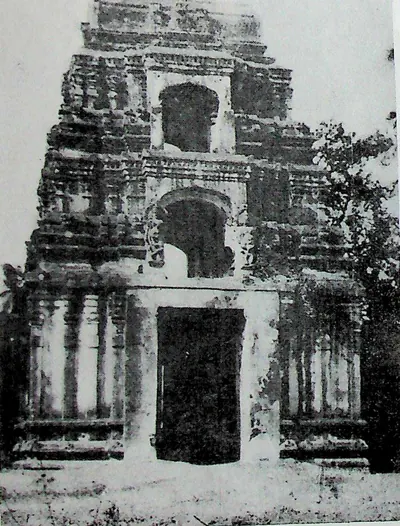 A massive weathered gateway tower with a large doorway at the base and arched openings above, with trees on both sides.