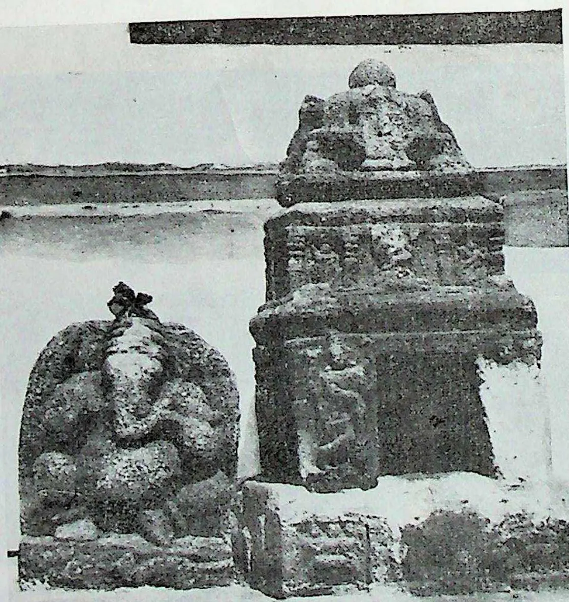 A miniature stone shrine with a domed top beside a seated Ganesha image, in front of a long wall.
