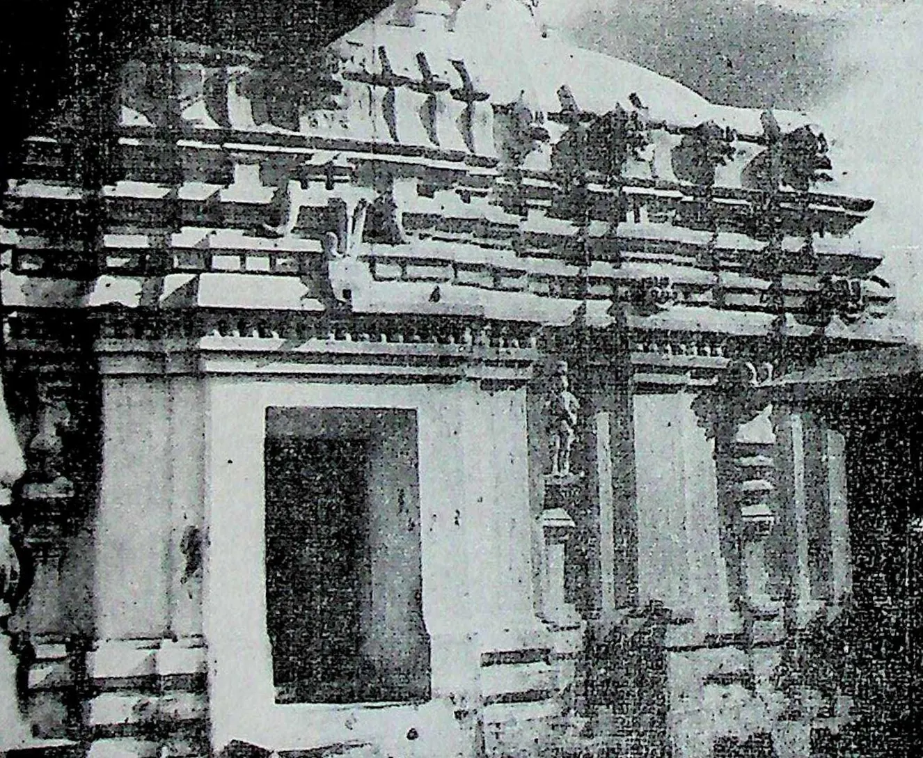 The south wall of a stone temple with a projecting doorway, pilasters and a cornice crowded with small roof mouldings and figures.