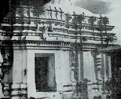The south wall of a stone temple with a projecting doorway, pilasters and a cornice crowded with small roof mouldings and figures.
