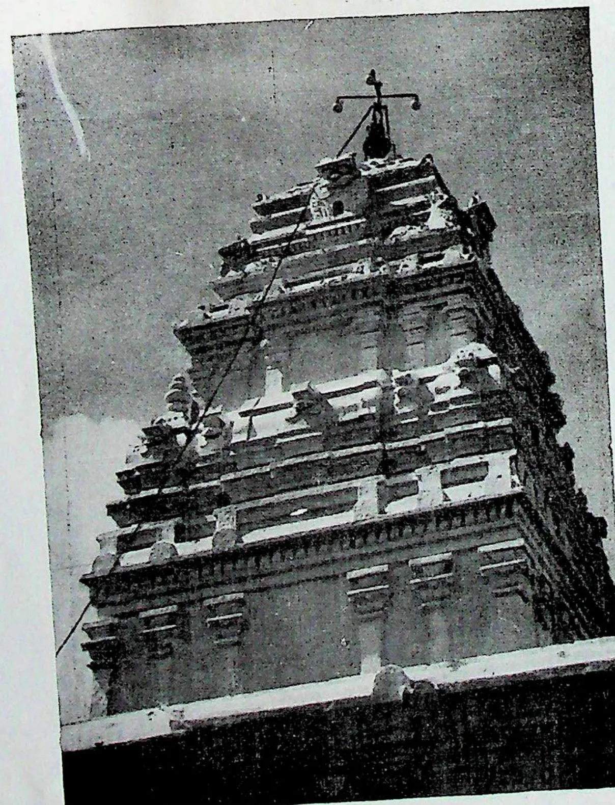 The tall stepped tower of a temple, plastered and crowded with mouldings, topped by a finial, seen from below against a dark sky.