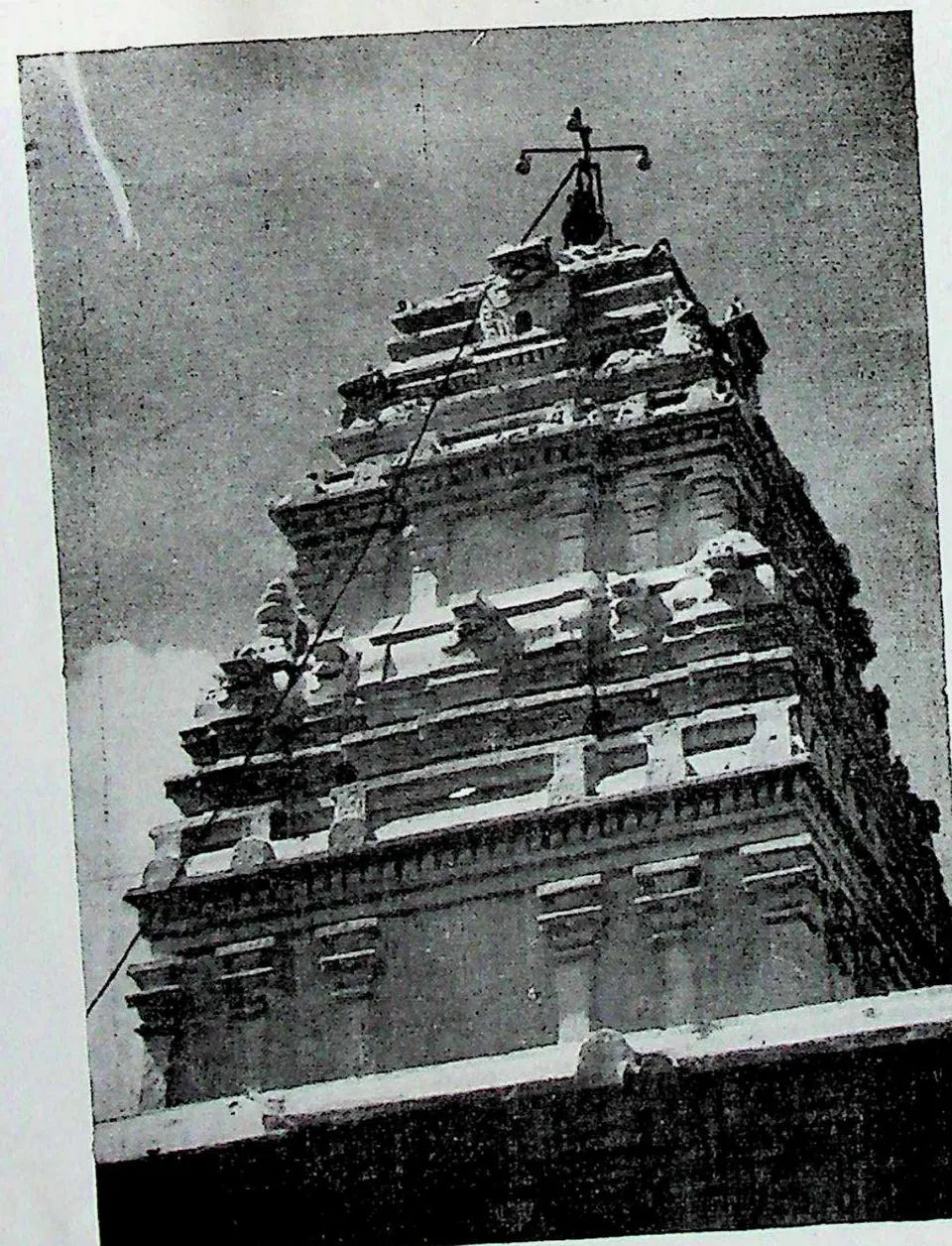 The tall stepped tower of a temple, plastered and crowded with mouldings, topped by a finial, seen from below against a dark sky.
