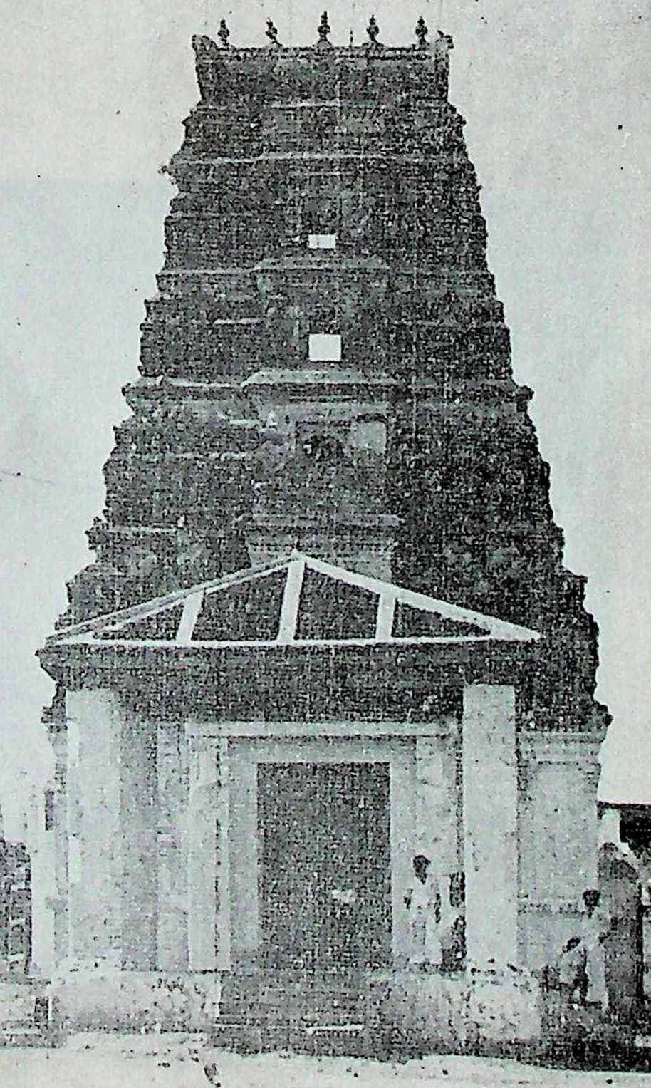 A tall gateway tower with a gabled roof over its doorway, people standing at its foot.