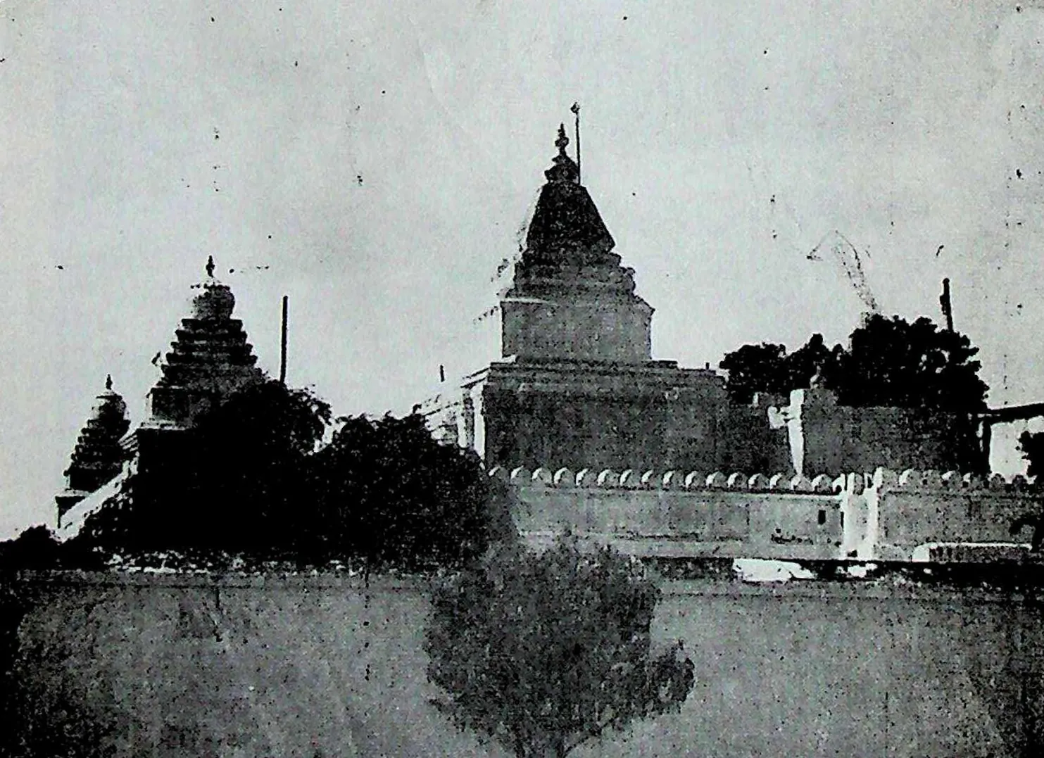 A long enclosure wall with a crenellated parapet, temple towers and trees rising behind it.