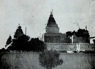 A long enclosure wall with a crenellated parapet, temple towers and trees rising behind it.