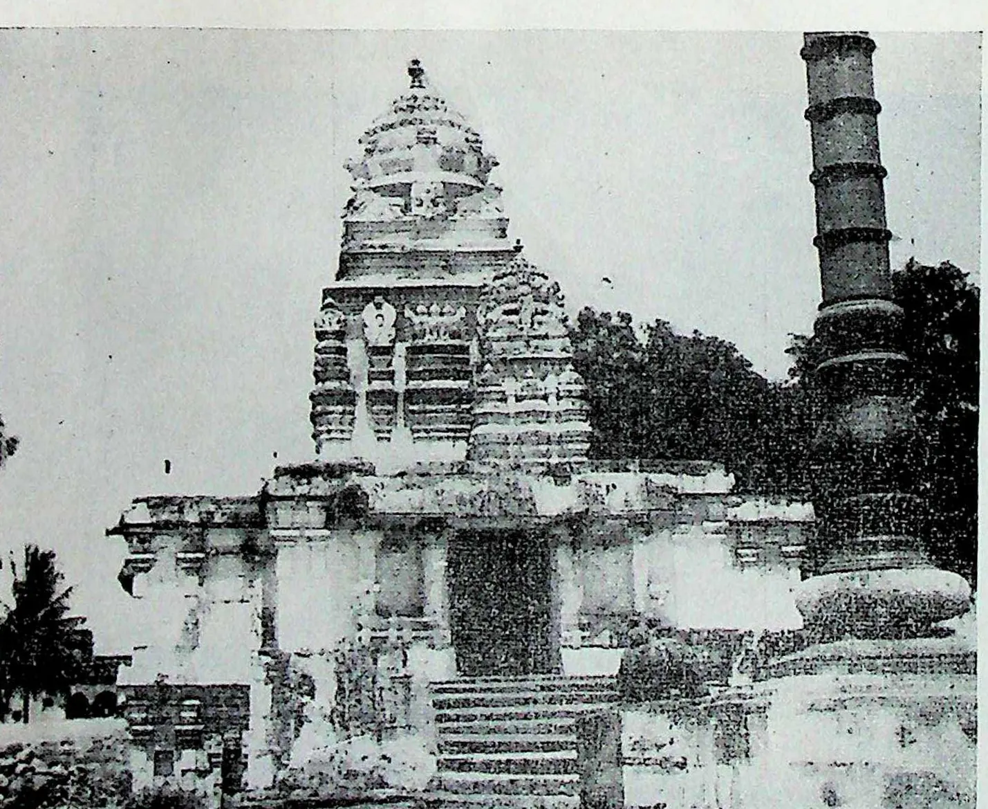 A temple with a tall tower and a front porch on a high platform reached by steps, a tall slender column at the right.