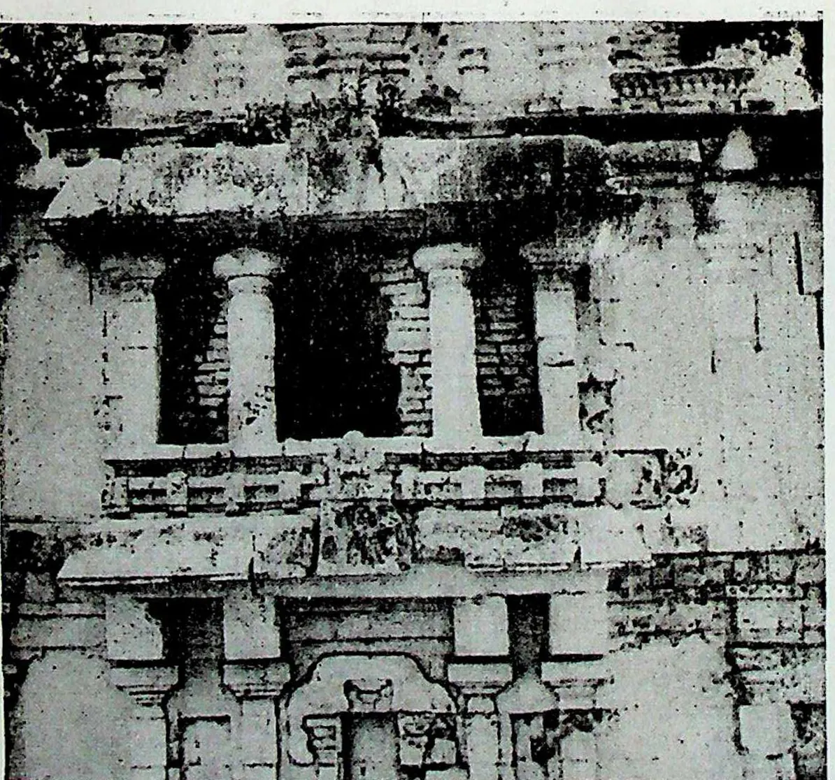 Close view of a temple wall with pilasters, a deep recessed balcony of short columns and carved panels.