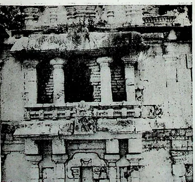 Close view of a temple wall with pilasters, a deep recessed balcony of short columns and carved panels.