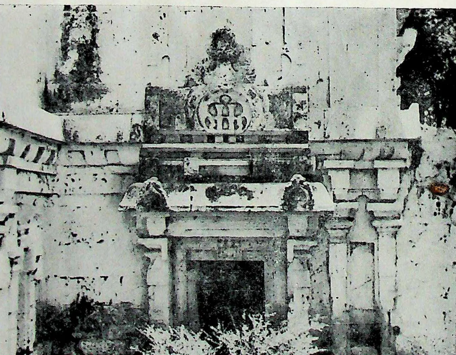 A projecting wall section with a framed doorway and an arched ornament above, the plaster stained and pitted.