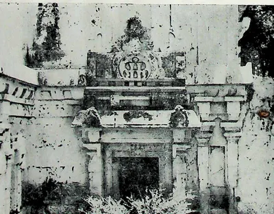 A projecting wall section with a framed doorway and an arched ornament above, the plaster stained and pitted.