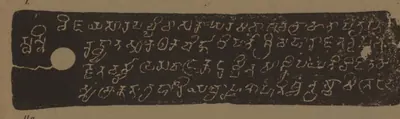 Lithograph of a narrow copper-plate face, pale letters on a dark grey ground: five lines of early box-headed letters with a white ring-hole at the left.