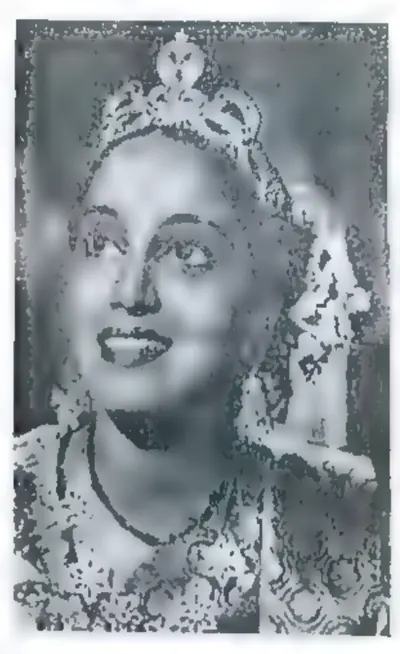 Black-and-white portrait of a smiling young woman wearing a tall jewelled crown and necklaces, looking up to the right.