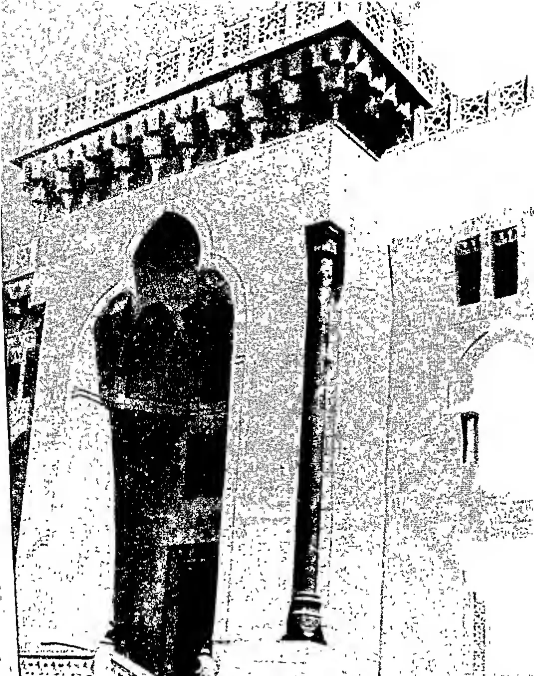 Grainy photograph of a stone building with a tall pointed-arch doorway, a pillar beside it and a deep carved cornice with brackets above.