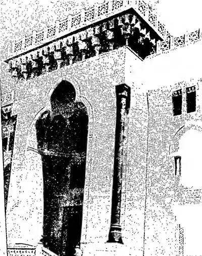 Grainy photograph of a stone building with a tall pointed-arch doorway, a pillar beside it and a deep carved cornice with brackets above.