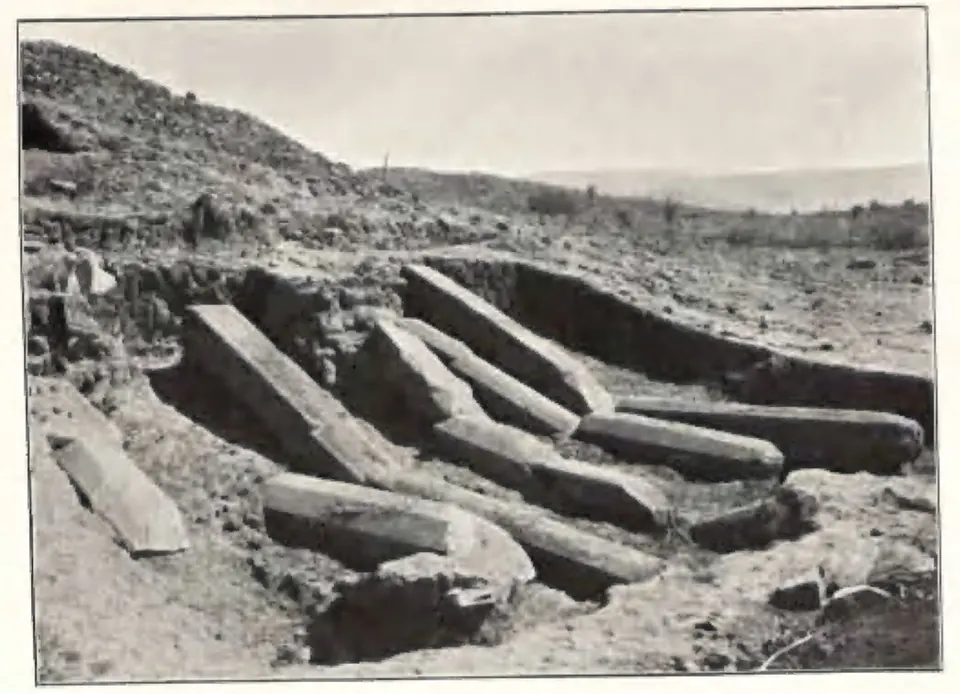Long fallen octagonal stone pillars lying in a trench beside the stupa, with bare hills behind.