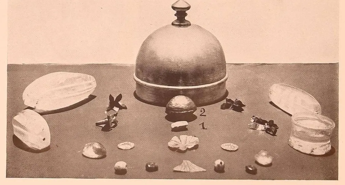 Relic objects laid out around a domed silver casket: a small gold box, beads, crystals and flowers of gold.