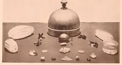 Relic objects laid out around a domed silver casket: a small gold box, beads, crystals and flowers of gold.