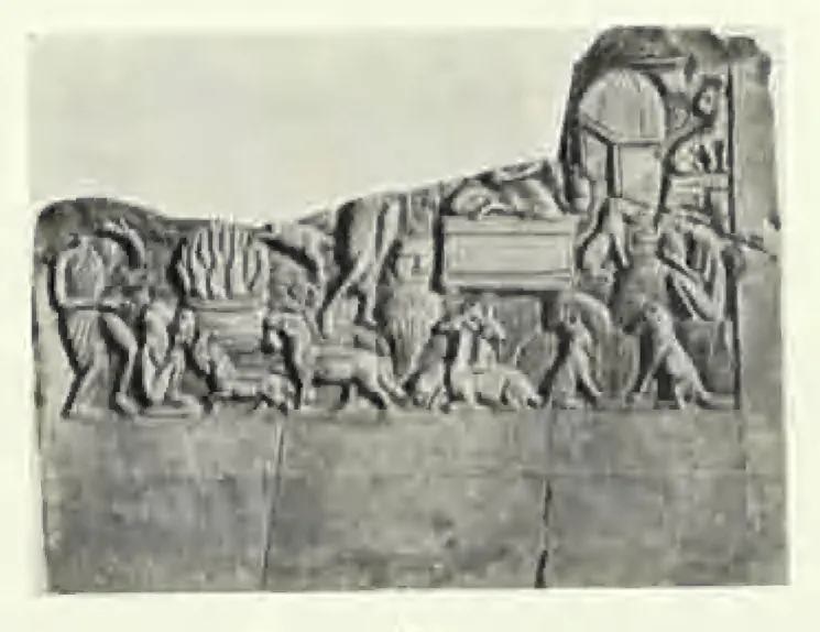 A broken carved slab with a frieze of small animals and human figures, a heap of flames at the left, a box-like seat in the middle and an arched hut at the upper right; the lower half of the stone is plain.