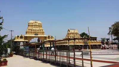 Two cream-and-gold tiered gateway towers rising above a long, low pillared hall, with a paved forecourt and metal queue railings in front.