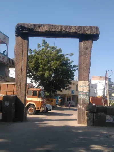 A tall stone gateway of two rough monolithic posts carrying a single heavy lintel, with a street, trucks and buildings beyond.