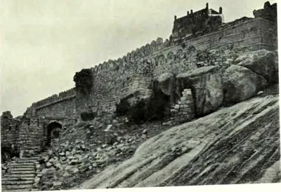 A battlemented stone wall climbing a sloping sheet of granite, with steps and a small gateway at the lower left.