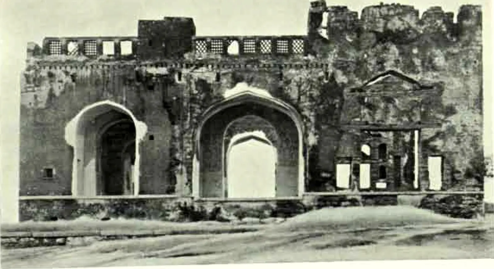 The ruined front of a building with three arched openings, a pedimented doorway at the right and a row of small openings along the top.