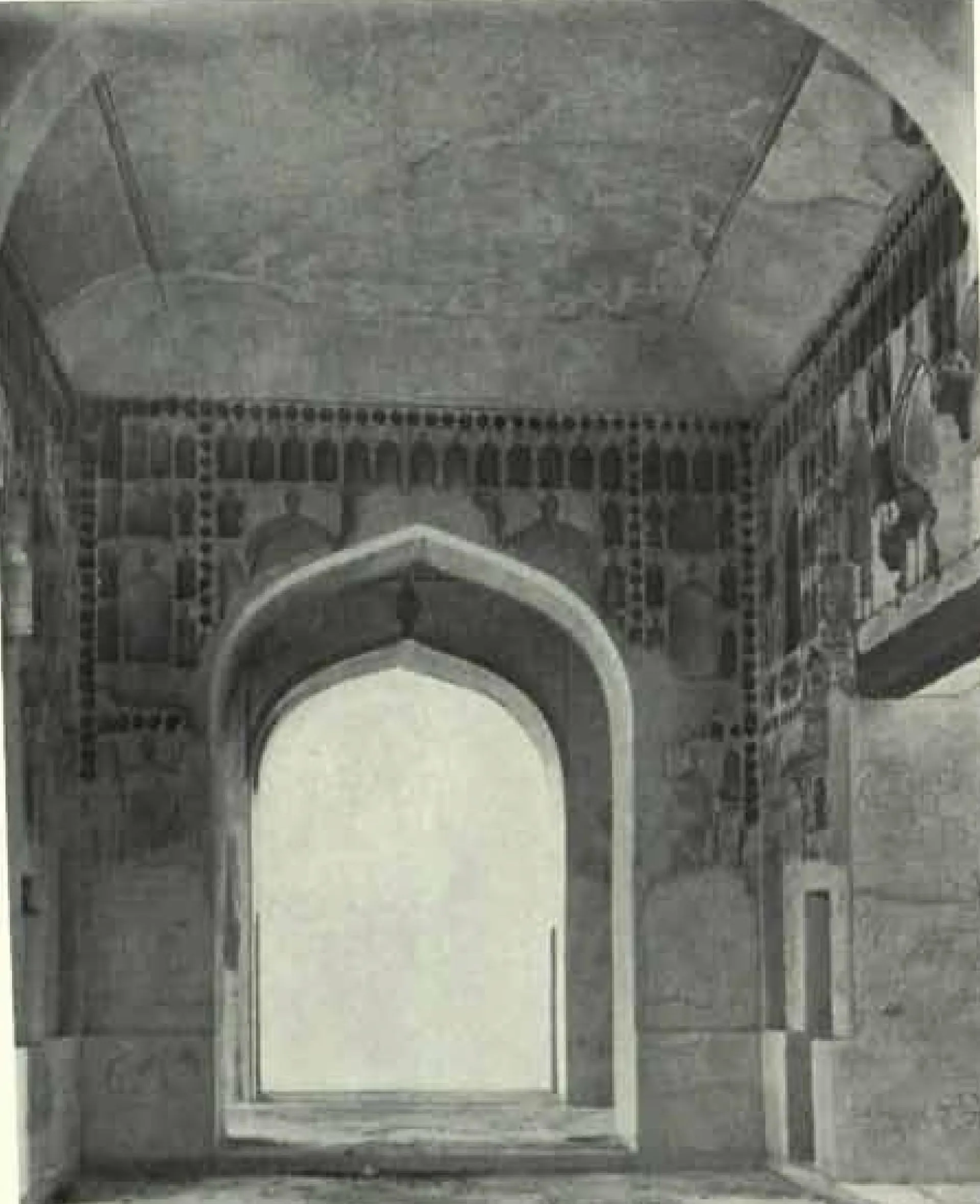 Inside a vaulted room: a pointed arch opens onto bright light, and the walls carry rows of small niches and traces of painted figures.