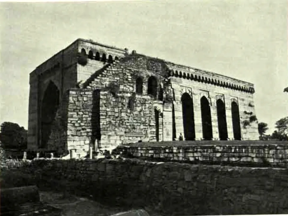 Shitab Khan's stone hall seen from the north-west: a tall arched end wall and a long side of pointed arches, on a terrace behind a rubble wall.