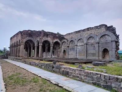 The partly ruined Konda Masjid: a long arcade of pointed arches on stone piers with collapsed upper walls, behind a paved path and a low rubble wall.