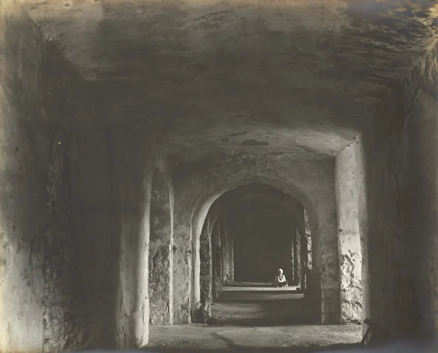 A long vaulted passage inside the ruined palace, with arched openings along both sides and a person standing at the far end.