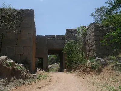 A dirt road running through a square stone gateway with a flat stone lintel, between high walls of large cut granite blocks.