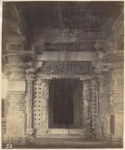 A dark shrine doorway framed by carved jambs and pierced stone screens, with heavy carved pillars and a carved lintel around it.