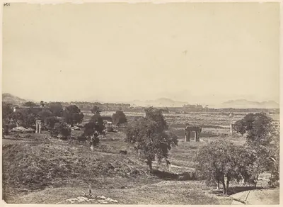 A wide view from a rocky hill over open fields and scattered trees, with stone gateways and pillars standing alone in the fields and low hills on the horizon.