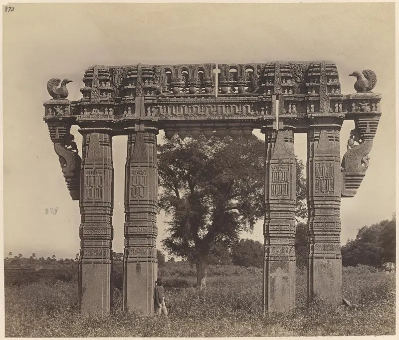 A four-pillared carved stone gateway with stone swans on the ends of its crossbeam, standing in grass with a tree behind it.