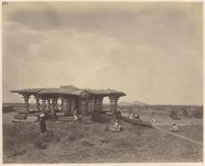 A flat-roofed stone pavilion on many pillars on a slight rise in open grassland, with people sitting and standing around it and hills on the horizon.