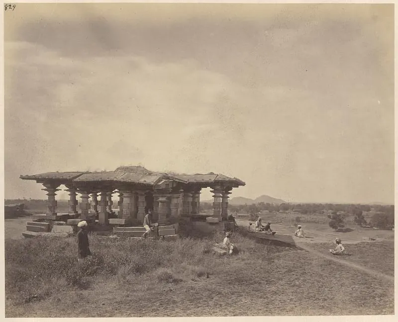 A flat-roofed stone pavilion on many pillars on a slight rise in open grassland, with people sitting and standing around it and hills on the horizon.