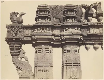 Close view of the carved crossbeam of a gateway: a stone swan on its end, a bracket with a rearing animal below it and a row of hanging stone buds under the beam.
