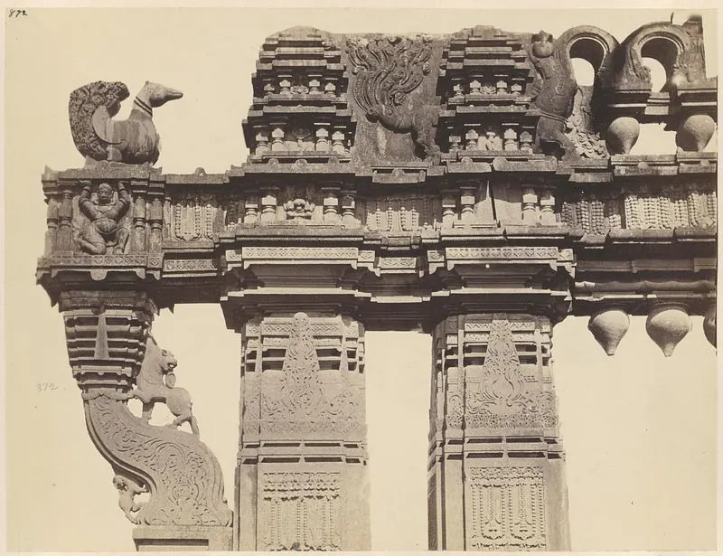 Close view of the carved crossbeam of a gateway: a stone swan on its end, a bracket with a rearing animal below it and a row of hanging stone buds under the beam.