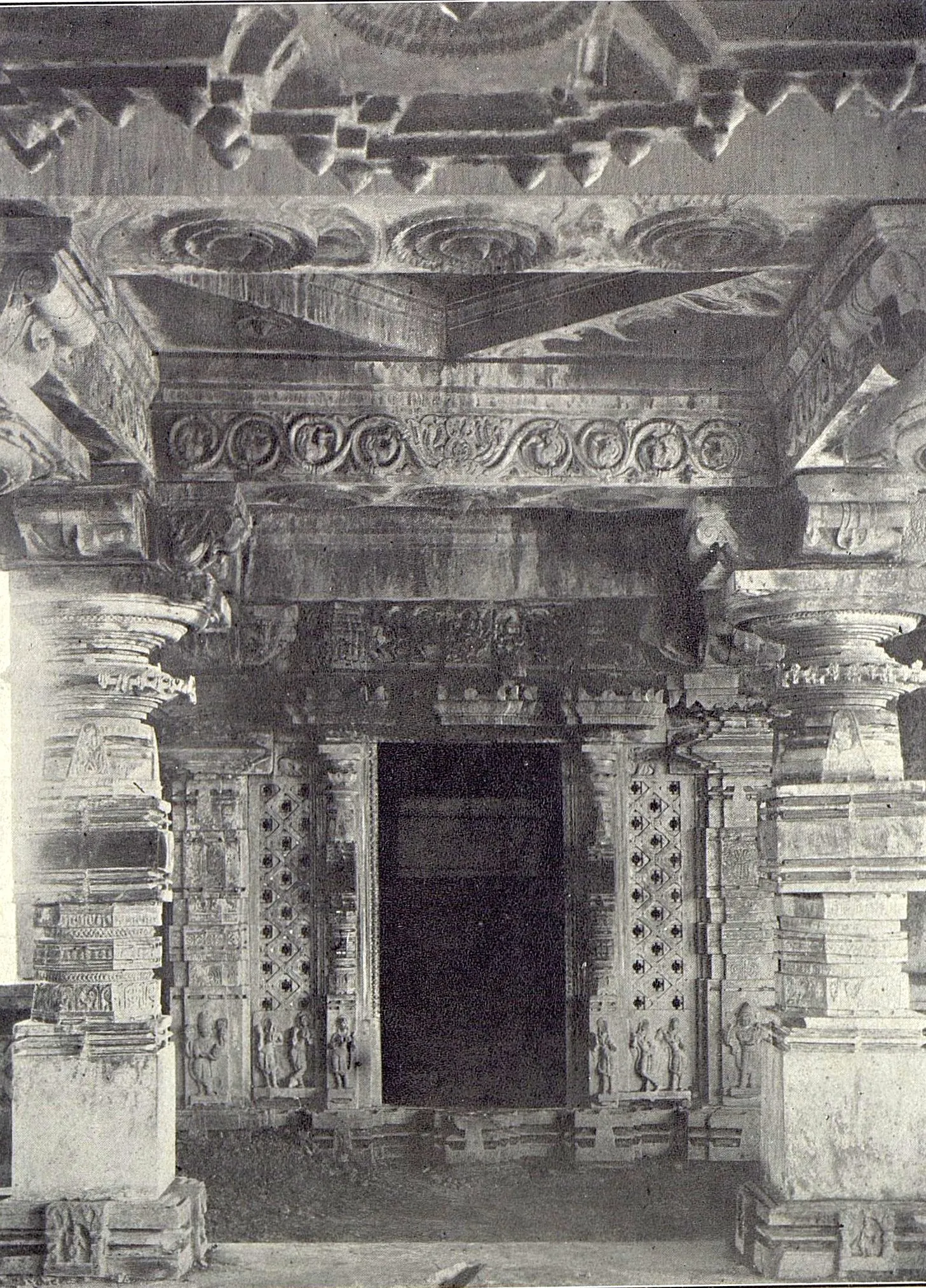 Inside a temple hall: a dark doorway with pierced screens on both sides, under carved beams and a ceiling of projecting brackets, between carved pillars.