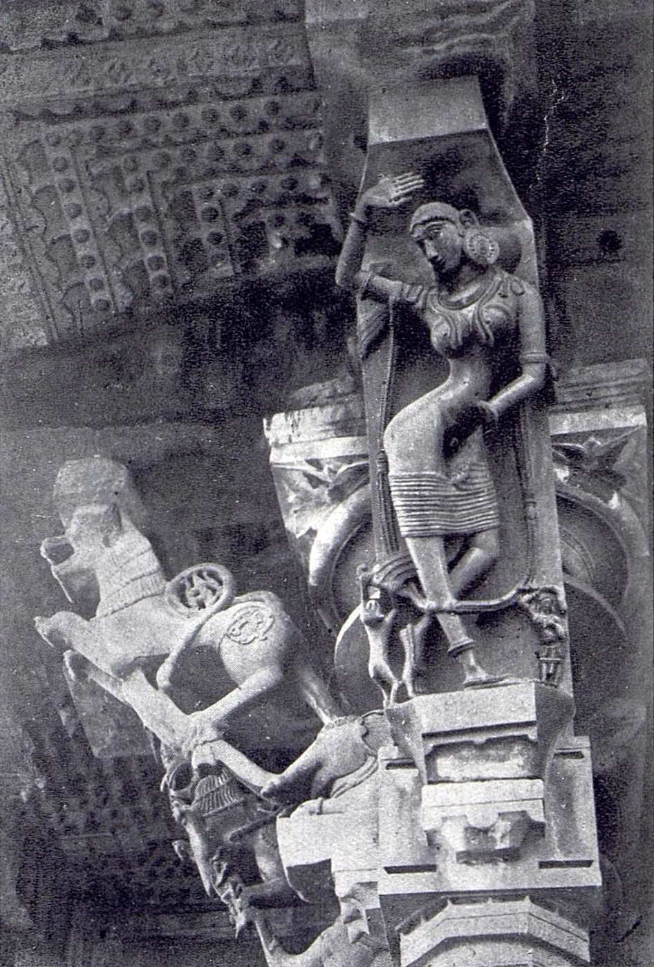 A slanting stone bracket carved with a standing woman, set above a pillar capital under the ceiling, with a rearing animal bracket beside it on the left.