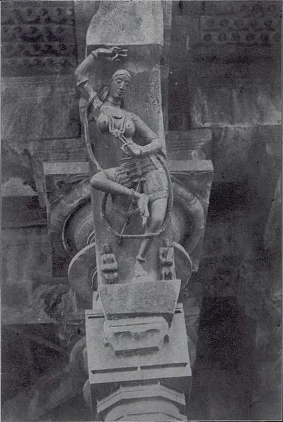 A slanting stone bracket carved with a dancer, one arm raised and a long looped cord or creeper around her body, with two small figures at her feet, above a pillar capital.