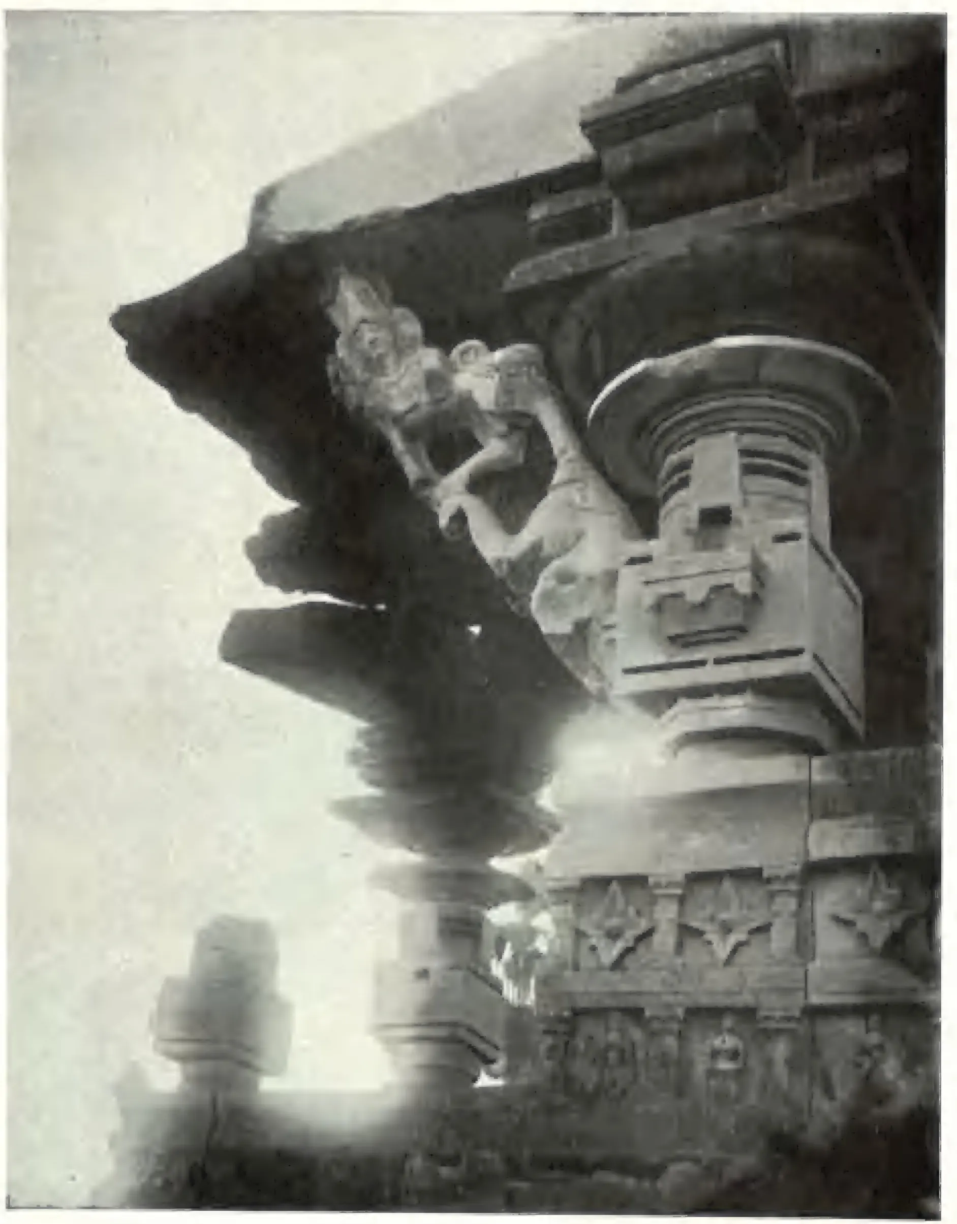 A dark stone bracket figure of a woman standing against a slanting bracket under the eave of the main Ghanpur temple, above a carved pillar capital and a moulded wall, lit from the side.