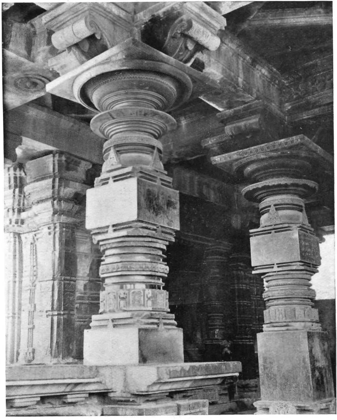Photograph inside a temple porch: massive lathe-turned stone pillars with ringed shafts and square bases, and carved beams overhead.