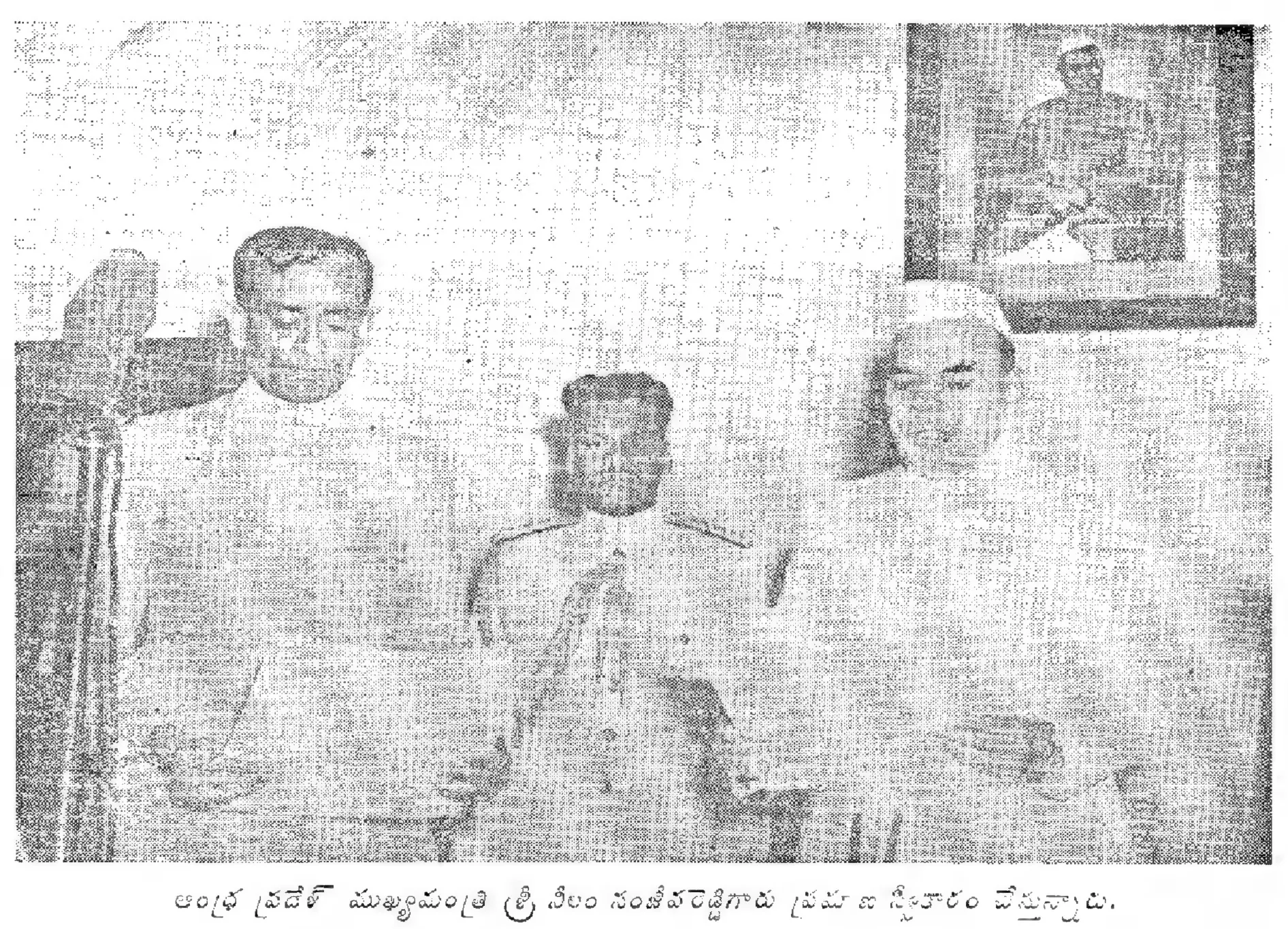 A grainy black-and-white photograph of three men standing in a room, the man on the left in a white coat reading from a paper at a microphone, an officer in uniform in the middle, and a framed portrait on the wall behind.