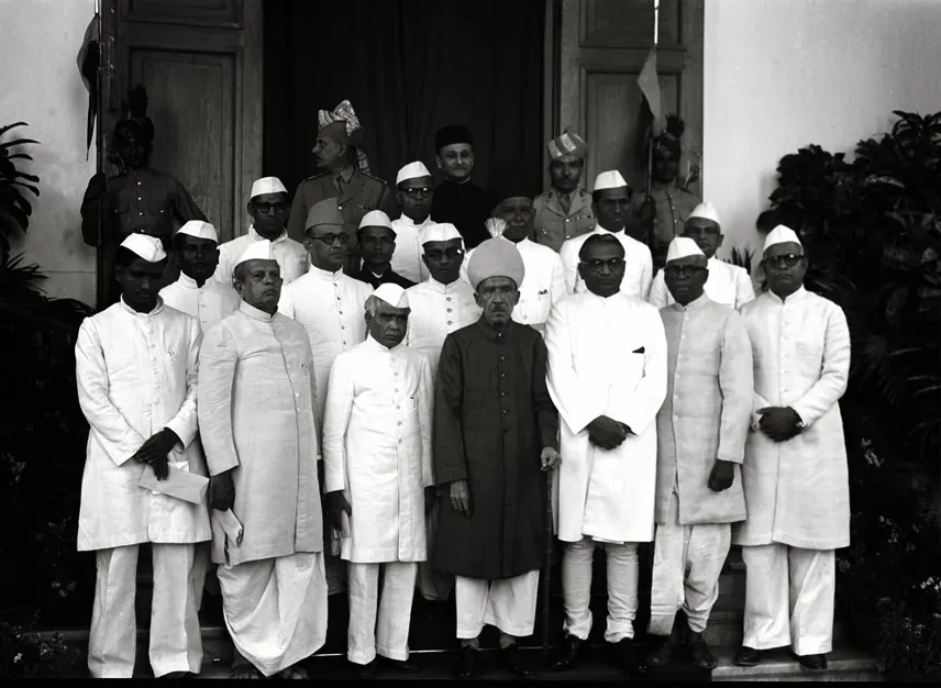 A black-and-white photograph of about twenty men, most in white caps and long white coats, standing in rows on the steps of a building, with one older man in a dark coat in the centre of the front row.