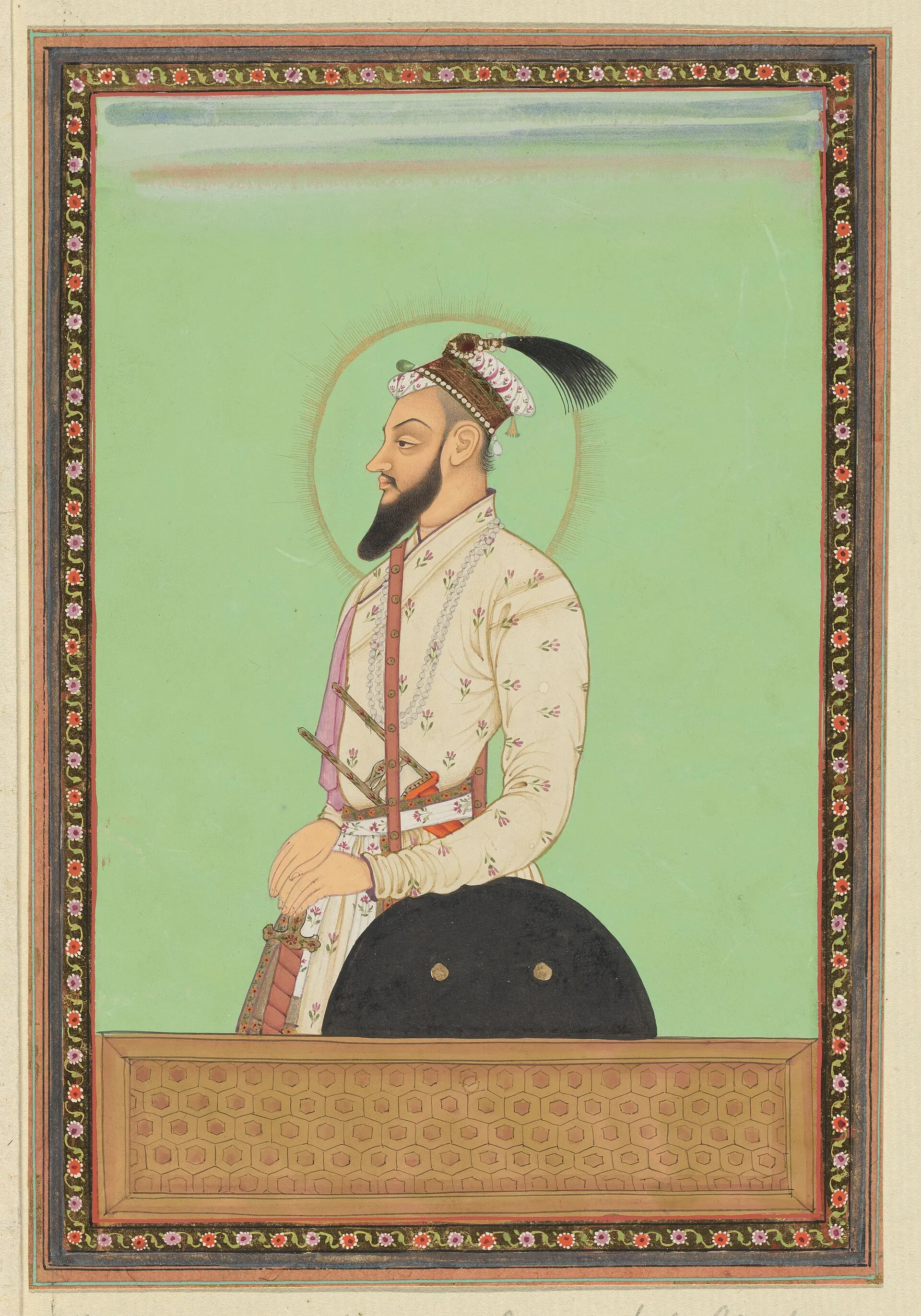 Deccani painting of a bearded man in a white patterned robe with a sword and shield, standing in profile with a halo against a green ground, in a decorated border.