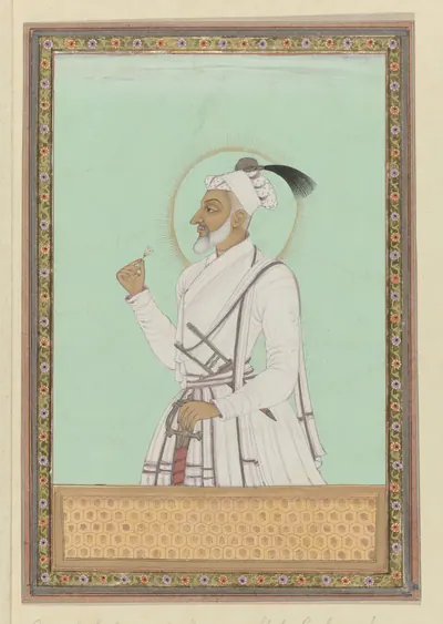 Deccani painting of an elderly white-bearded man in white robes and turban, standing in profile with a halo against a pale green ground, in a decorated border.